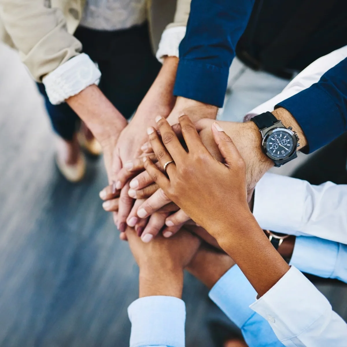 Hände mehrerer Personen, die sich übereinander legen, symbolisieren Teamarbeit und Zusammenhalt.