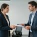 Zwei Personen im Büro, die sich Dokumente reichen.